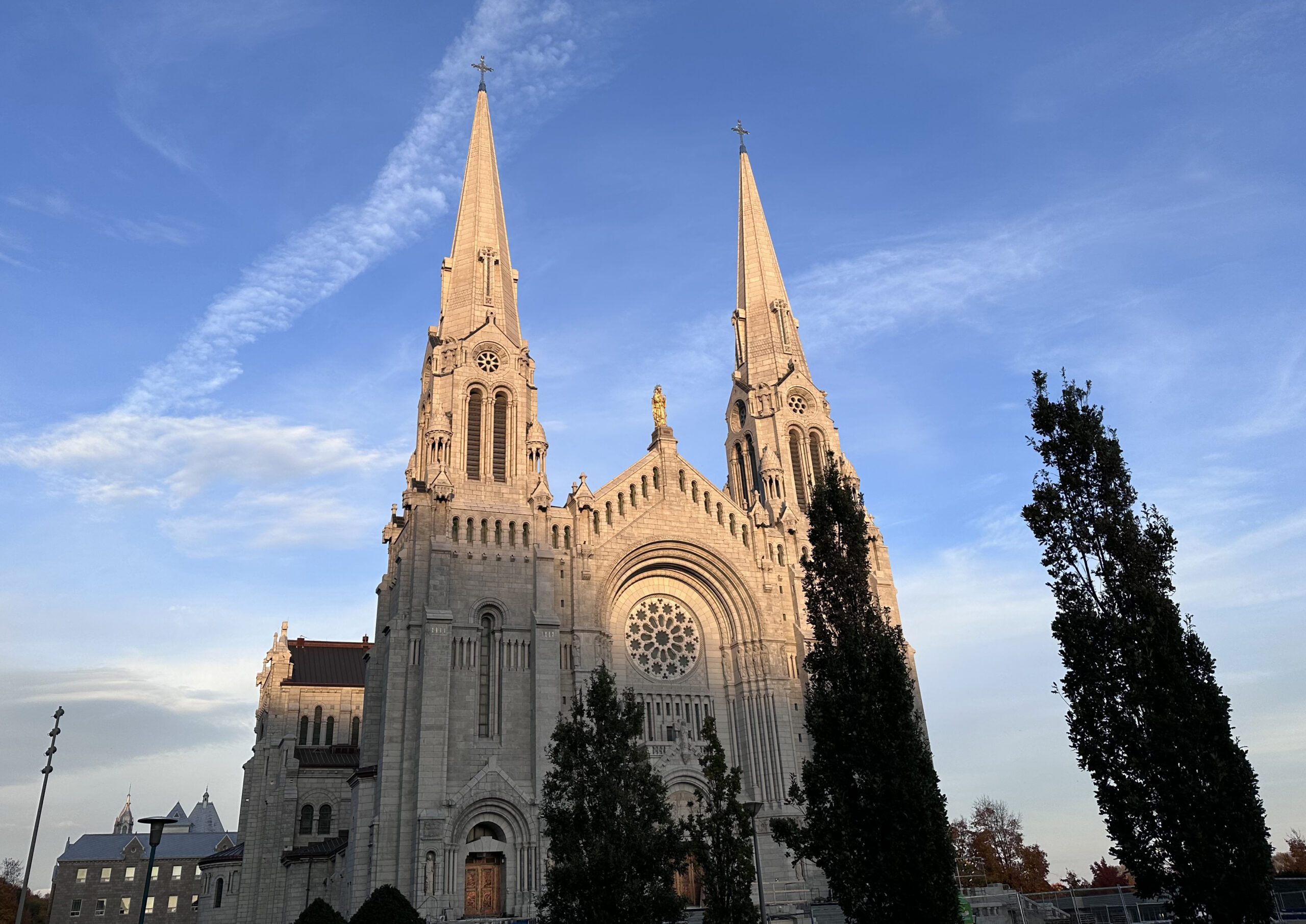 Vue en contre-plongée de la basilique Sainte-Anne-de-Beaupré en pierre claire, avec ses deux grands clochers à flèche se découpant sur un ciel bleu ensoleillé.