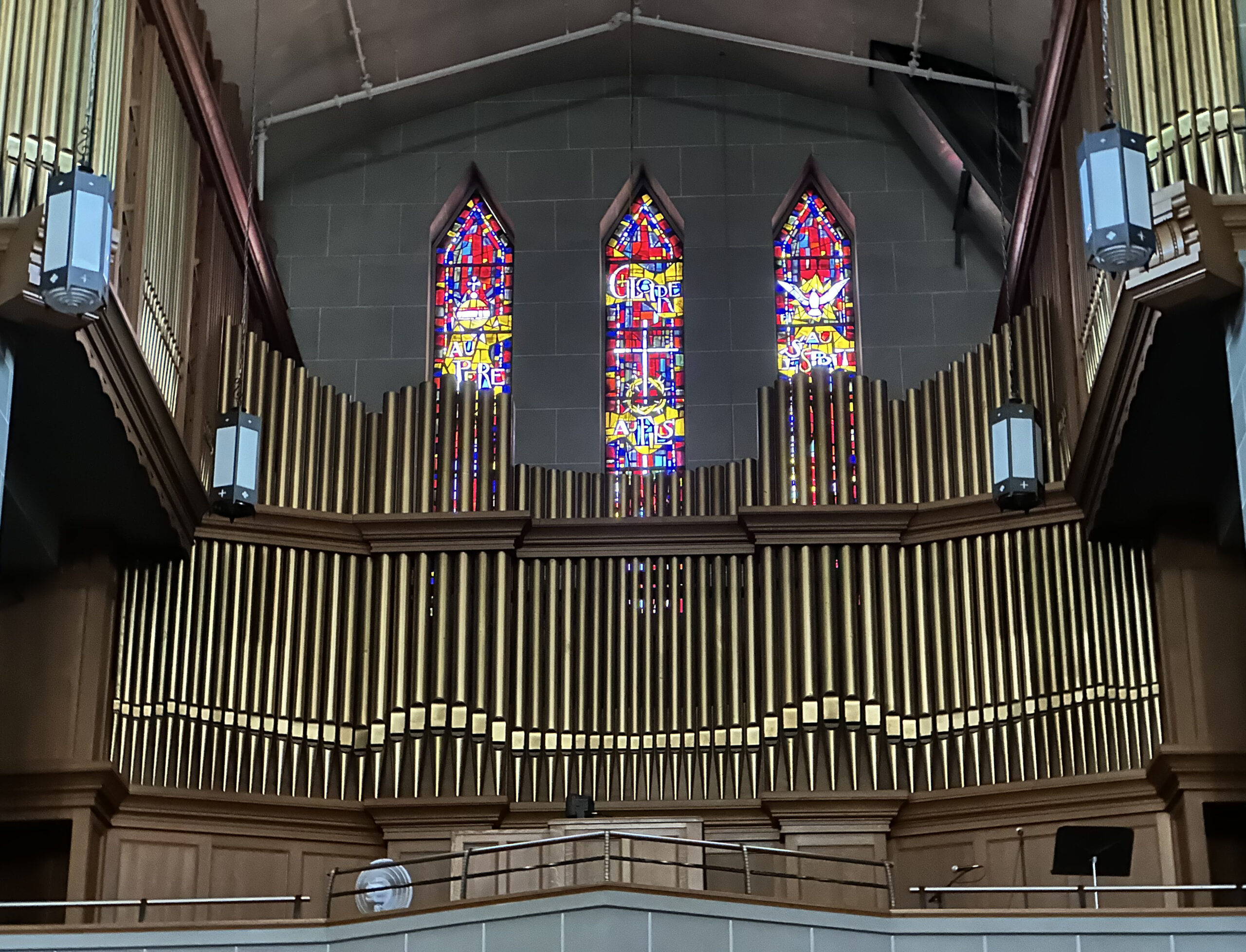 Grand orgue de la cathédrale Notre-Dame-de-l’Assomption à tuyaux dorés surmonté de trois vitraux lancettes aux couleurs vives rouges, bleues et jaunes encastrés dans le mur de pierre.