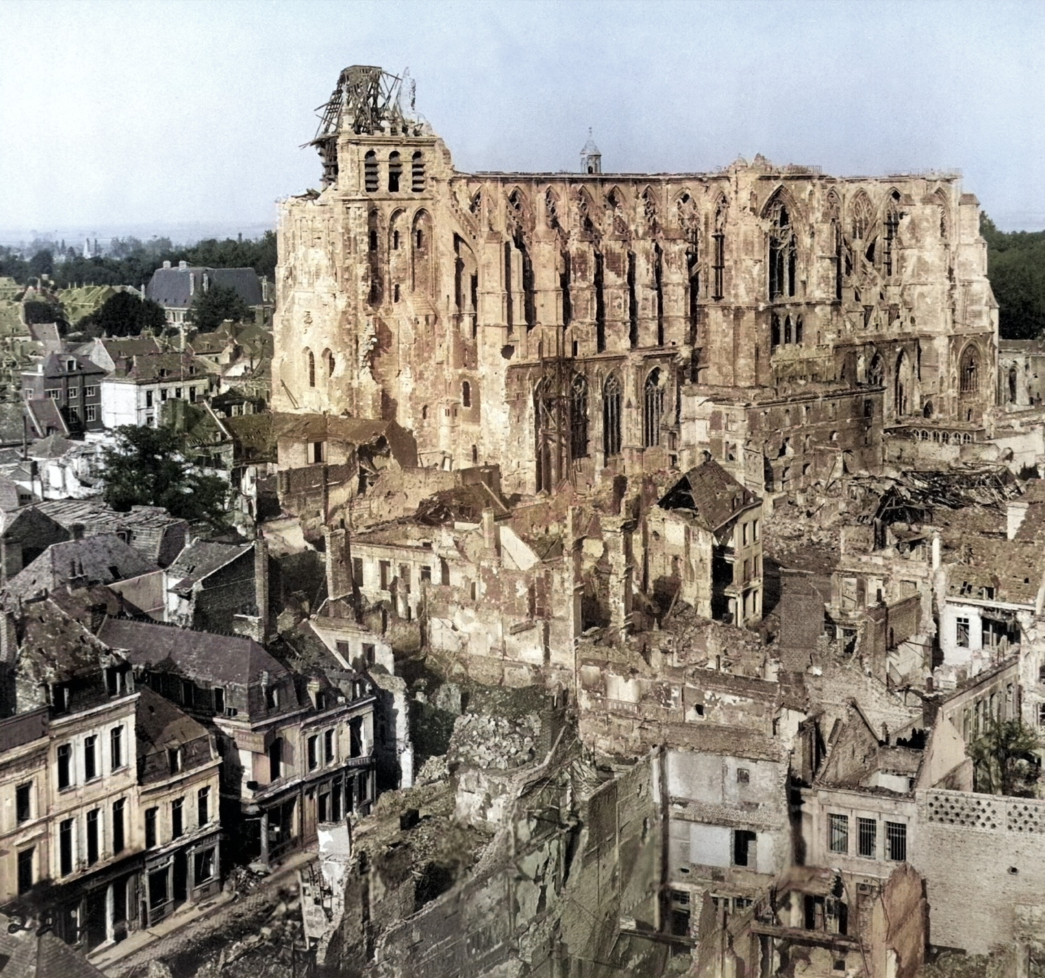 Photographie montrant la basilique de Saint-Quentin grand édifice gothique fortement endommagée par des bombardements, entourée d'un quartier d'habitations en ruines et dévasté.