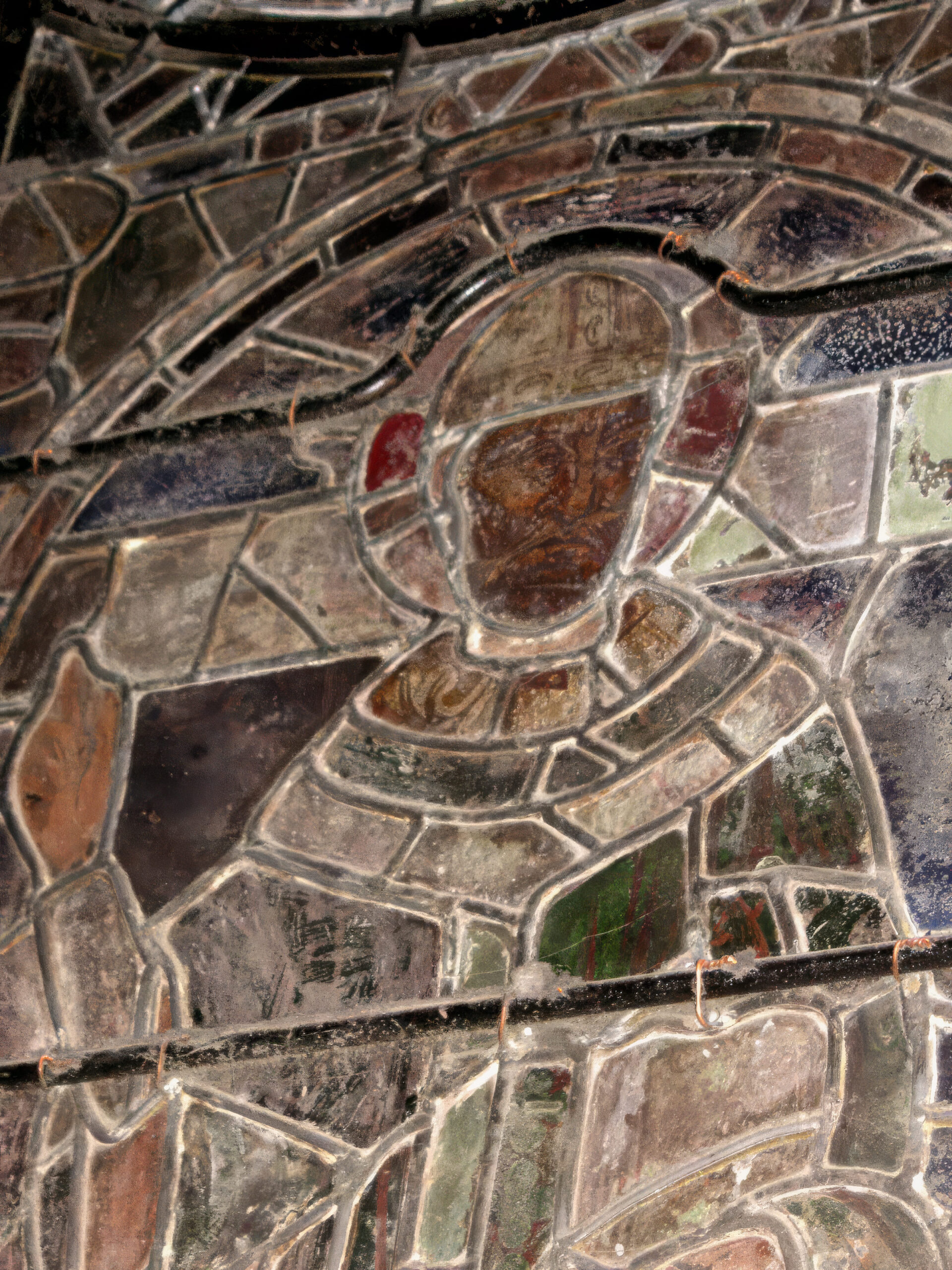 Gros plan sur un vitrail figuratif ancien représentant un saint nimbé, composé de pièces de verre peintes à la grisaille et assemblées par des baguettes de plomb renforcées de vergettes métalliques.
