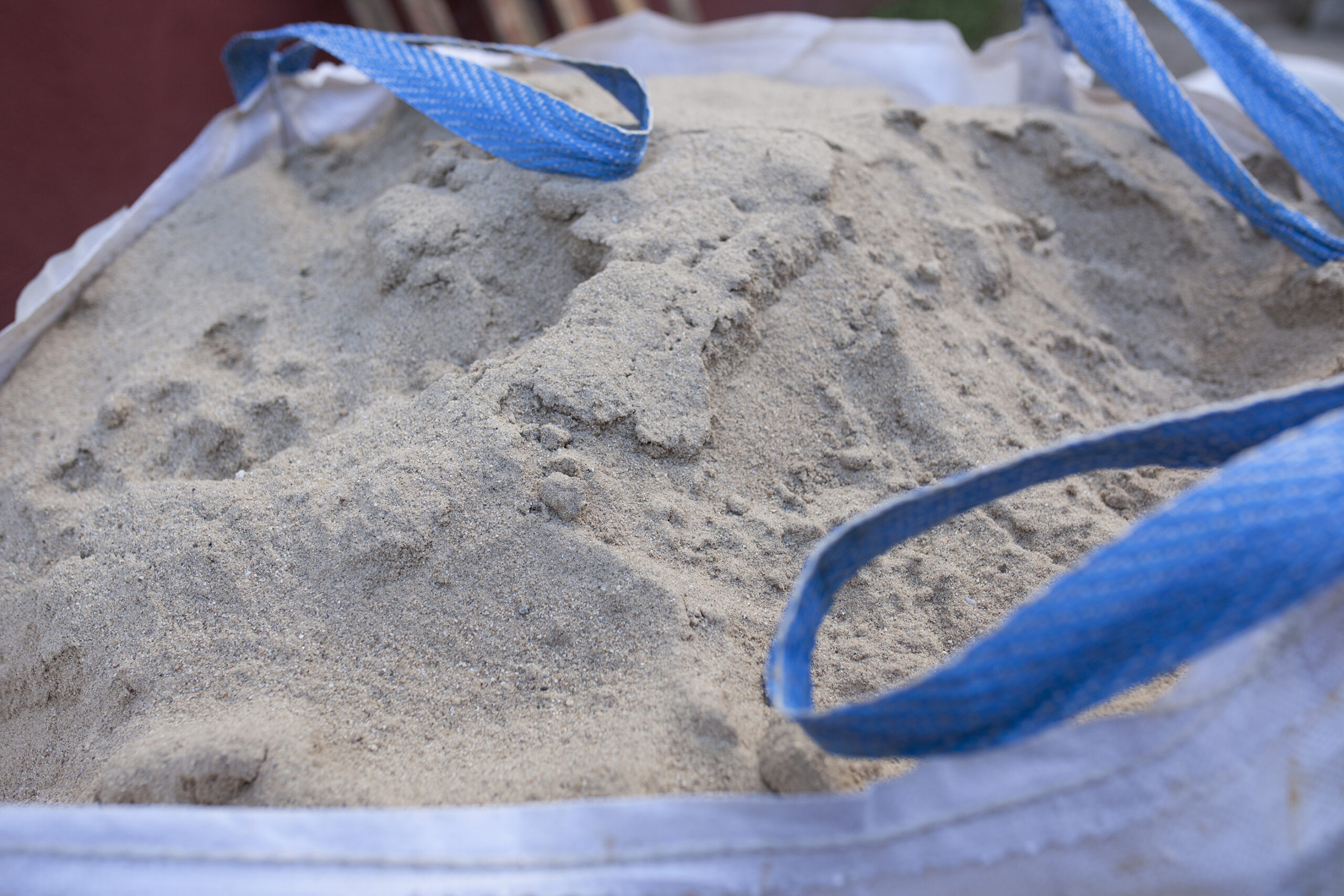 Gros plan sur un grand sac de chantier à sangle bleue contenant du sable ou de la poudre de ciment utilisée pour couler la structure en ciment des dalles de verre.